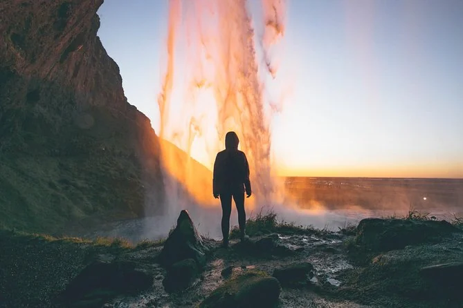 A silhouetted person behind Seljalandsfoss with the setting sun glowing through the falling water